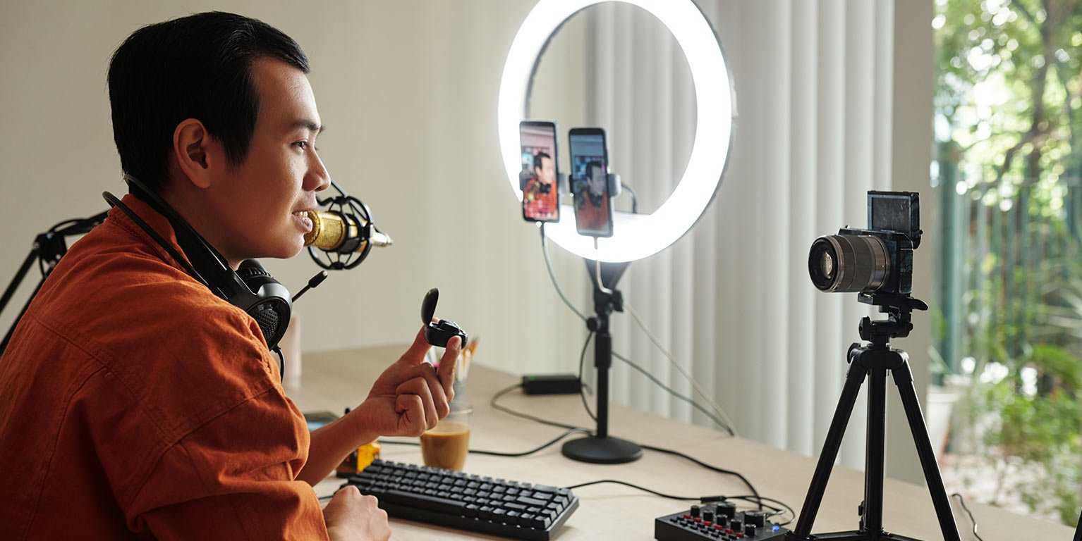 Homme asiatique qui utilise un studio webdiffusion portatif avec un ring light, une caméra et un cellulaire.
